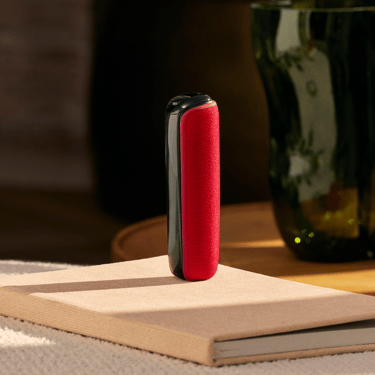 Ploom AURA z tylną okładką w kolorze Lava Red położoną na książce na stole.
